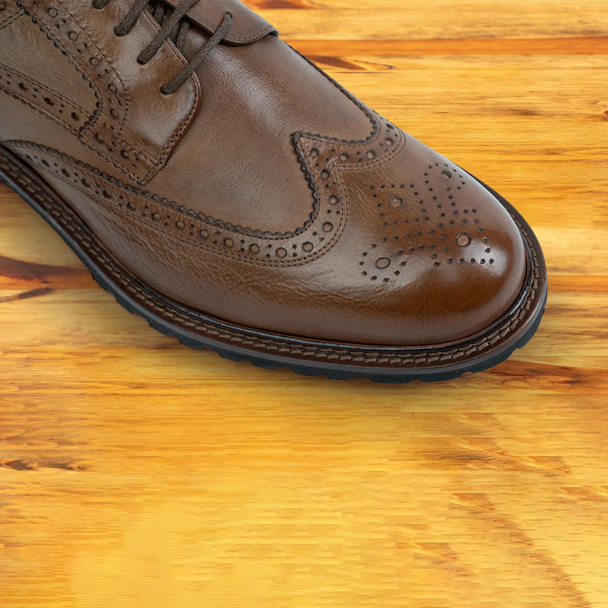 A close-up of a Cerris leather wingtip derby shoe with brogue detailing and a black sole, shown from a front angle on a wooden table.