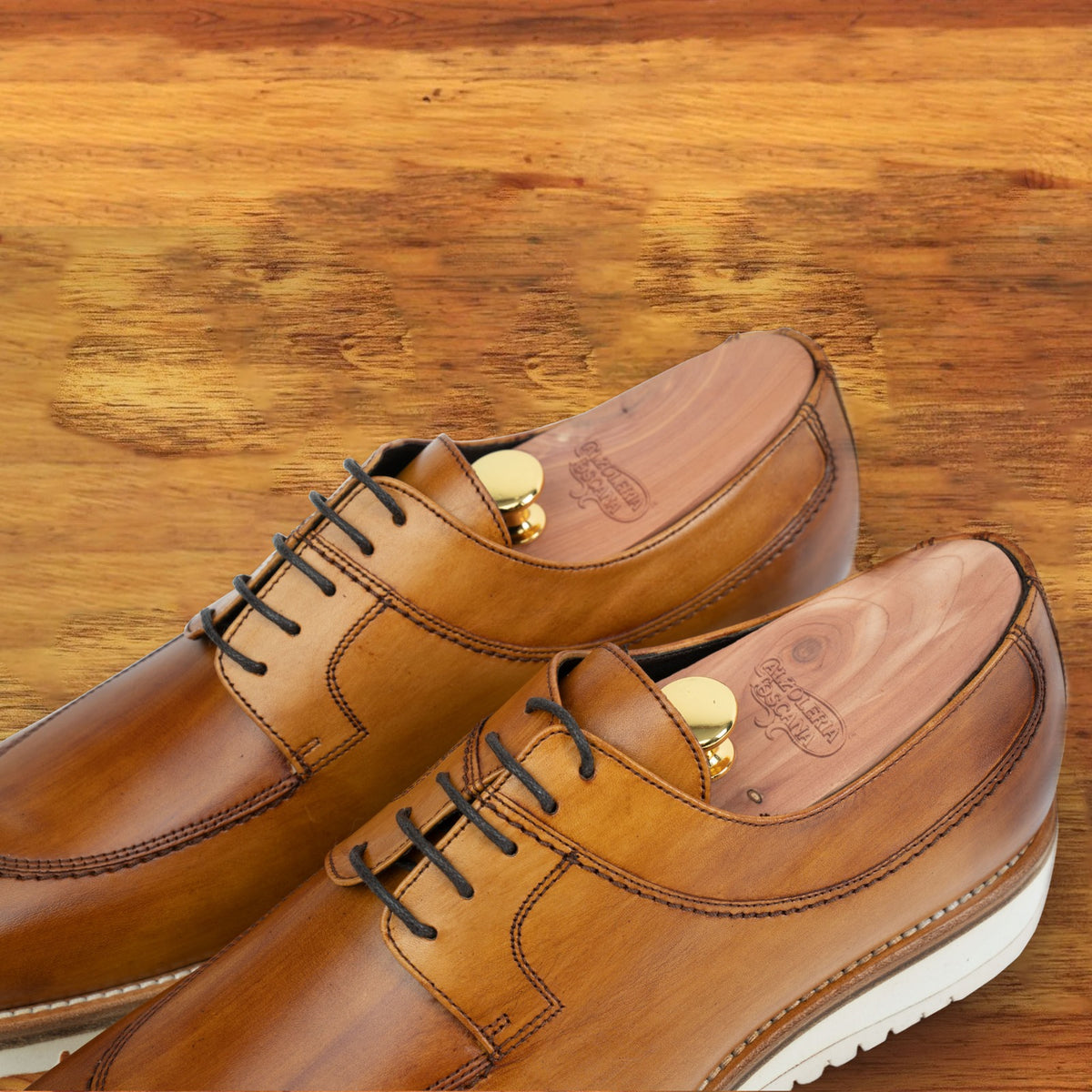 Q907 Dark Caramel leather shoes, pair viewed from above showing the burnished finish, cedar shoe trees and white midsole on a wooden surface