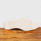 Q907 Dark Caramel leather sneaker, close-up of the ridged cream outsole on a wooden surface with a light gray background