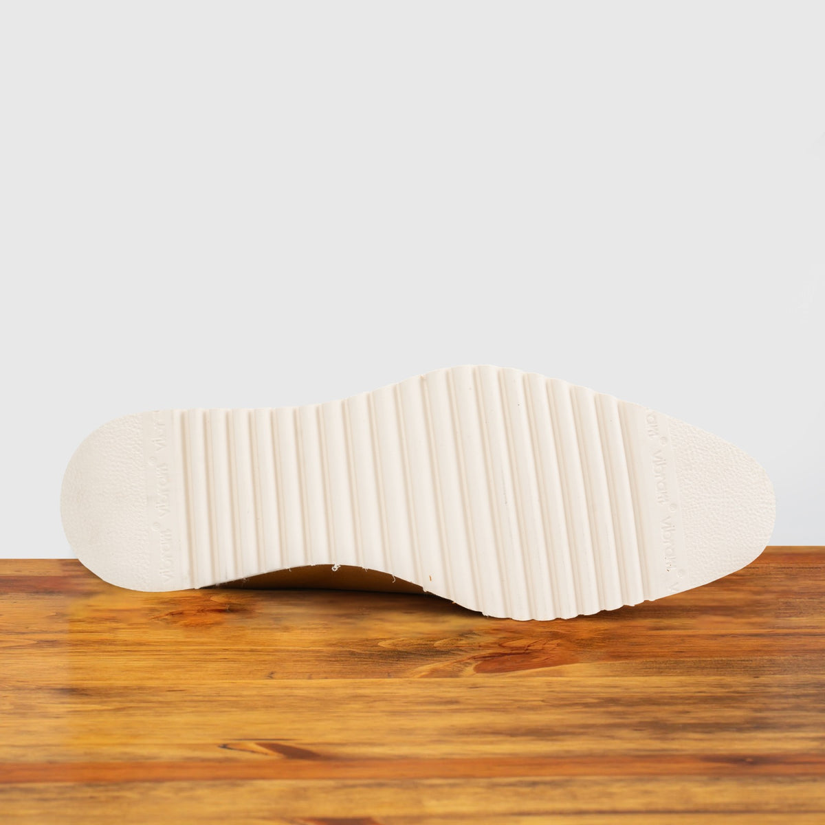 Q907 Dark Caramel leather sneaker, close-up of the ridged cream outsole on a wooden surface with a light gray background