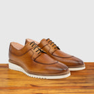 A pair of Dark Caramel leather shoe on a wooden surface with a light gray background