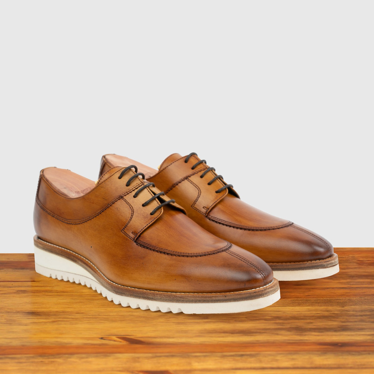 A pair of Dark Caramel leather shoe on a wooden surface with a light gray background
