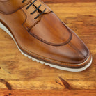 Q907 Dark Caramel leather shoe, close-up of the toe and lacing showing the burnished finish, white midsole and welted sole on a wooden surface