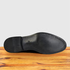 The  leather outsole of a dress shoe, shown from a top-down view resting on a wooden surface against a light gray background.