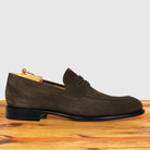 A dusty brown suede penny loafer shoe displayed on a wooden surface against a light gray background.