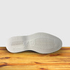 Outsole of Navy blue suede loafer with a rubber sole positioned on a wooden surface.