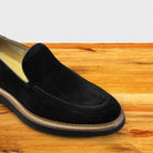 Black Venetian loafer with a rubber sole positioned on a wooden surface.