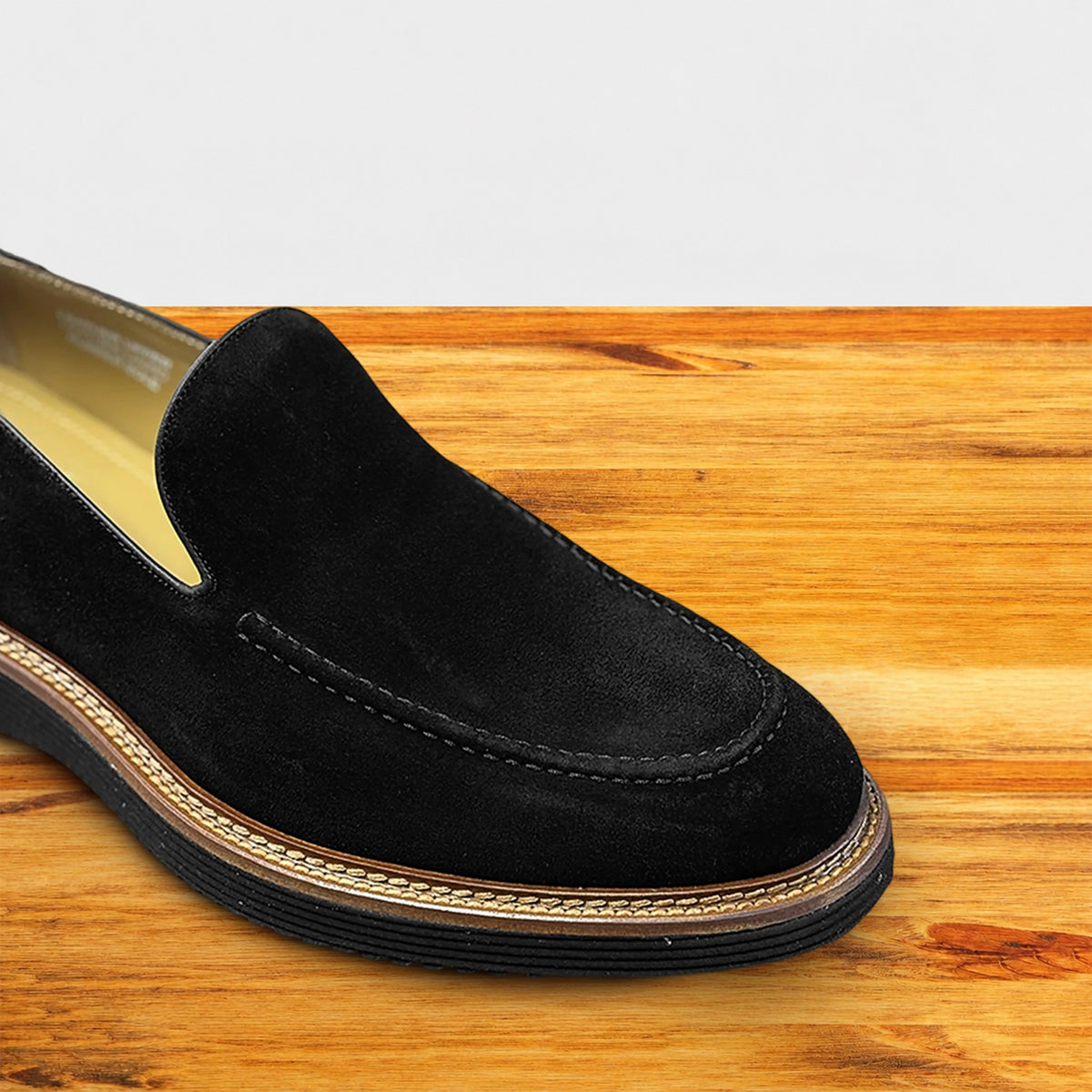 Black Venetian loafer with a rubber sole positioned on a wooden surface.