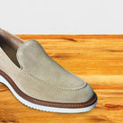 A single Cream slip-on loafer in light taupe suede with a brown welt and white sole, shown on a wooden surface