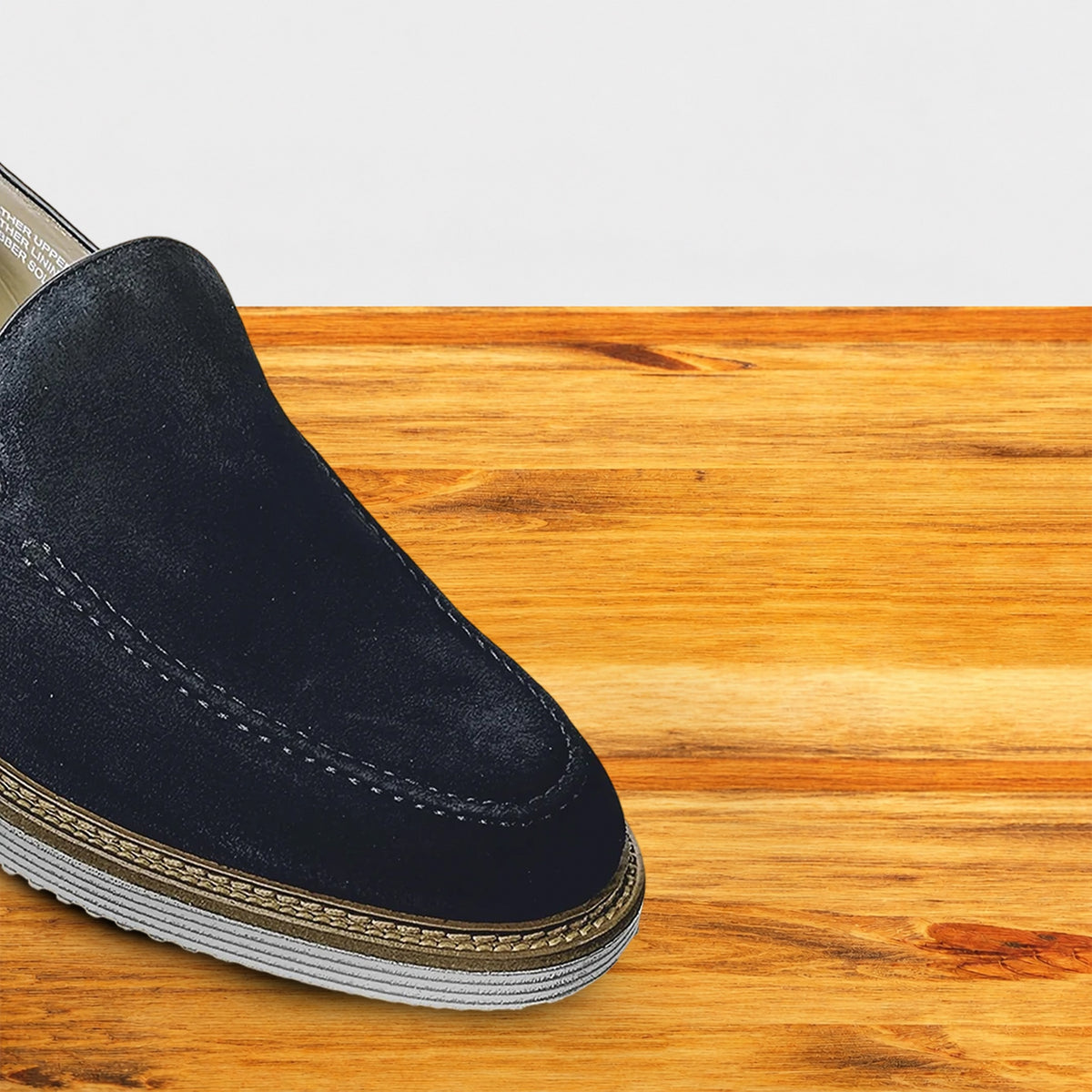 Navy blue suede loafer with a rubber sole positioned on a wooden surface.