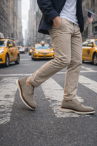 Person walking on a city street wearing A pair of Cashmere color suede shoes with taxis in the background