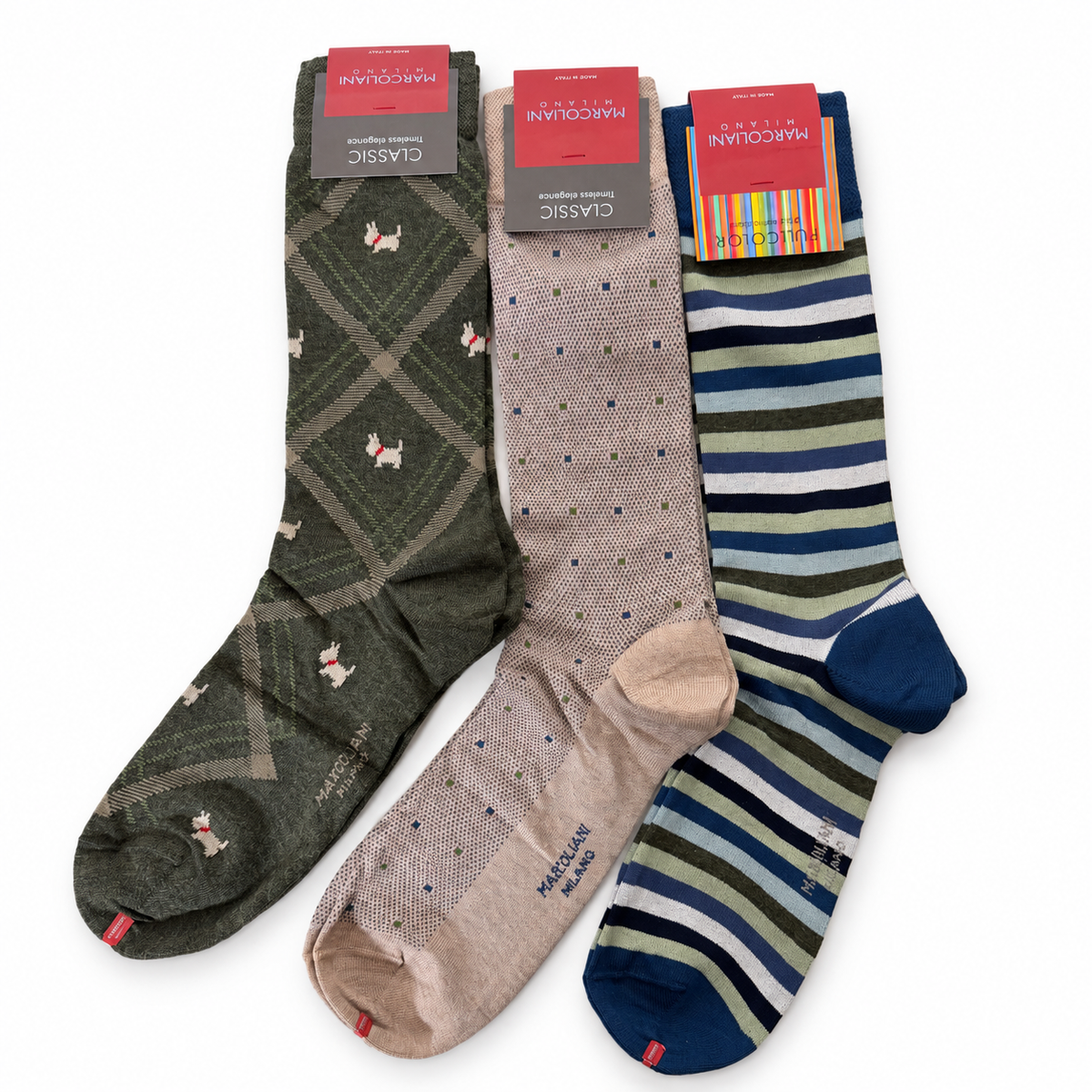 Three pairs of Marcoliani dress socks: olive green argyle with white dog motifs, beige with small blue and green squares, and blue, green, and white stripes.