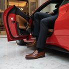 Man in a suit and brown shoes getting into a red car in an indoor setting.