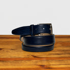 A dark navy blue leather belt with a silver-tone metal buckle, neatly coiled on a rustic wooden surface against a clean white background.