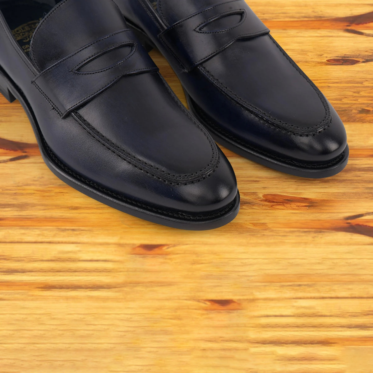 A Pair of Navy blue Italian leather dress loafer with a penny strap, on a wooden surface.