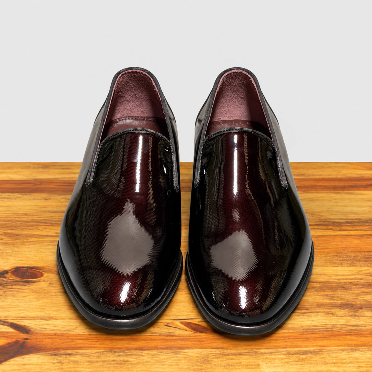 A pair of Burgundy patent leather slip-on dress loafers with black soles, shown from a front