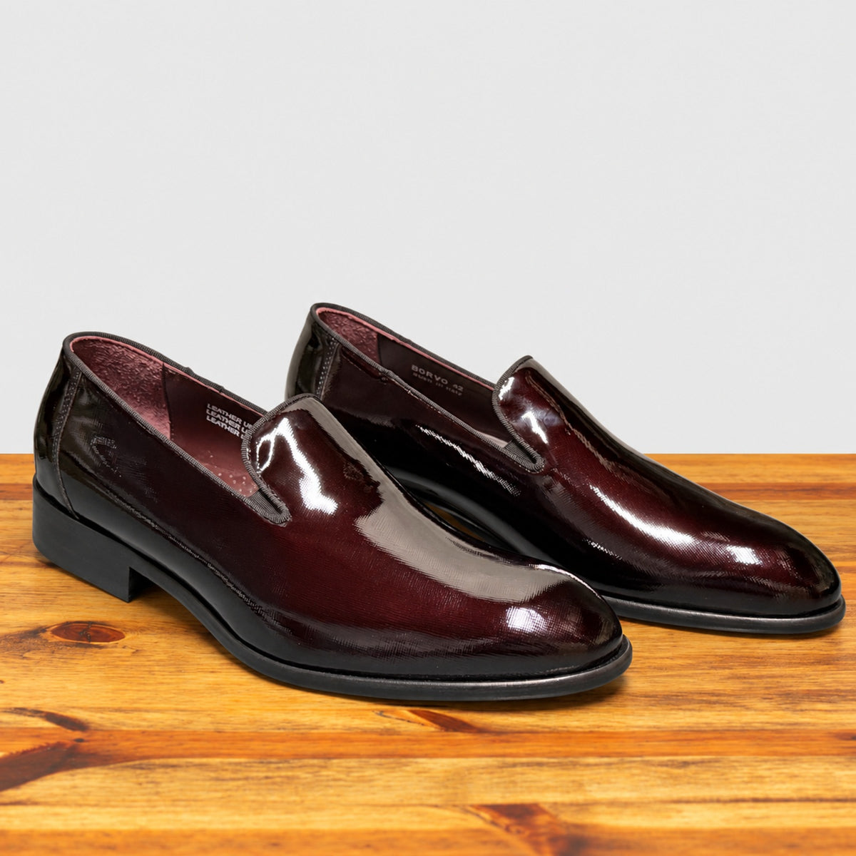 A pair of Burgundy patent leather slip-on dress loafers with black soles, shown from a front three-quarter angle.