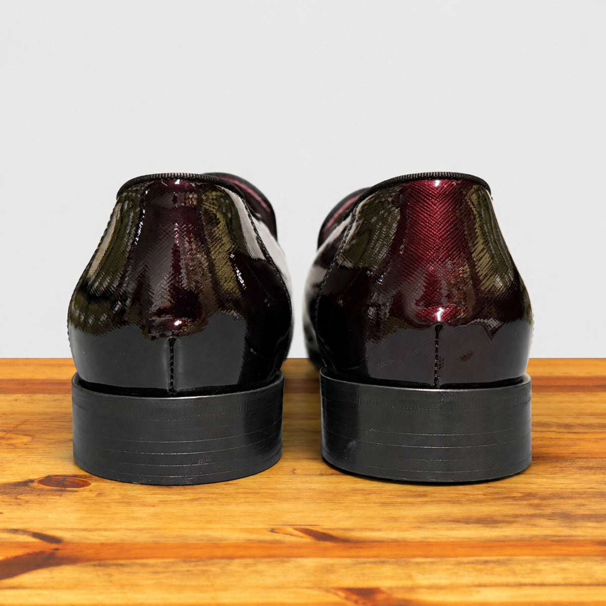 A pair of Burgundy patent leather slip-on dress loafers with black stacked heels, shown from the back.