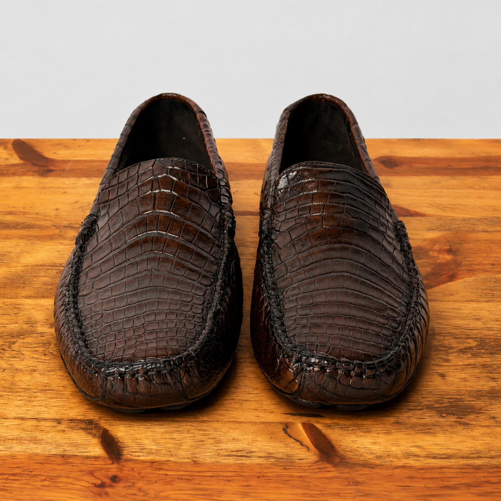 A pair of cerris color crocodile-slip-on loafers displayed on a wooden surface against a light gray background.