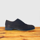 A Dusty Brown color suede Oxford cap-toe shoe with a leather sole, displayed on a wooden surface.