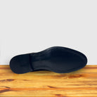 Outsole of  Dusty Brown color suede Oxford cap-toe shoe with a leather sole, displayed on a wooden surface.