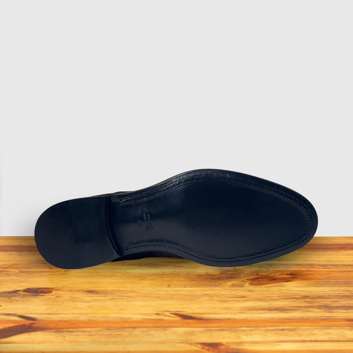 Outsole of  Dusty Brown color suede Oxford cap-toe shoe with a leather sole, displayed on a wooden surface.