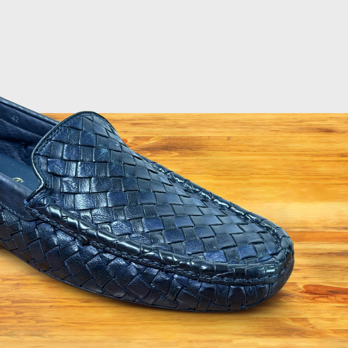 Close view of Navy Blue loafer shoe with woven pattern on a wooden surface