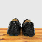 A pair of burgundy crocodile-embossed loafers with chunky block soles , shown from the back on a wooden surface against a light gray background.