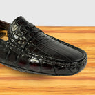 A burgundy crocodile-embossed leather loafer shown in a close-up side view, resting on a light wood surface against a white background.