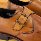 Brown leather shoe with a buckle detail on a wooden surface