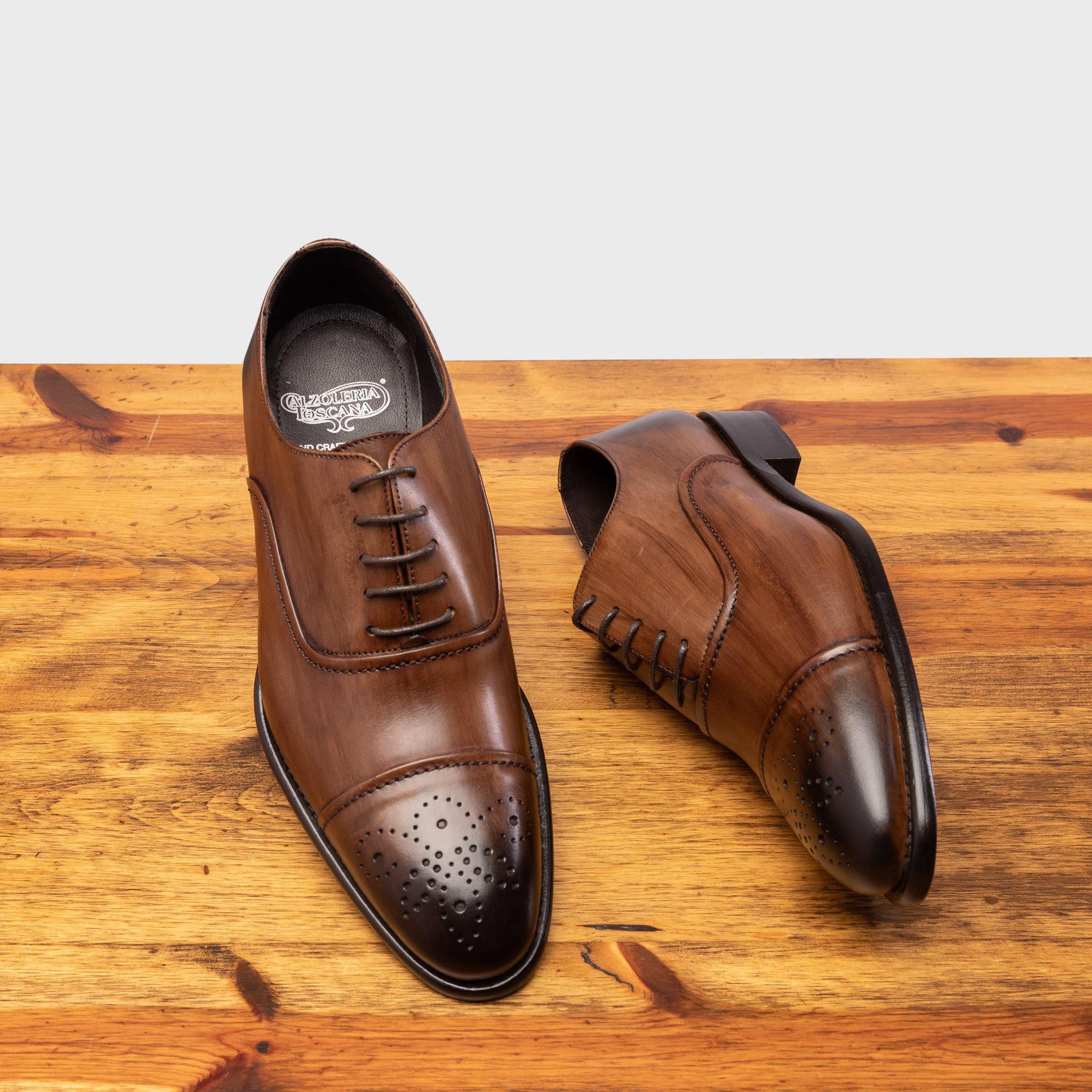 Picture showcasing the 2361 Calzoleria Toscana Brown  Cayenne Calf Cap-Toe pair with the brand name insole on top of a wooden table