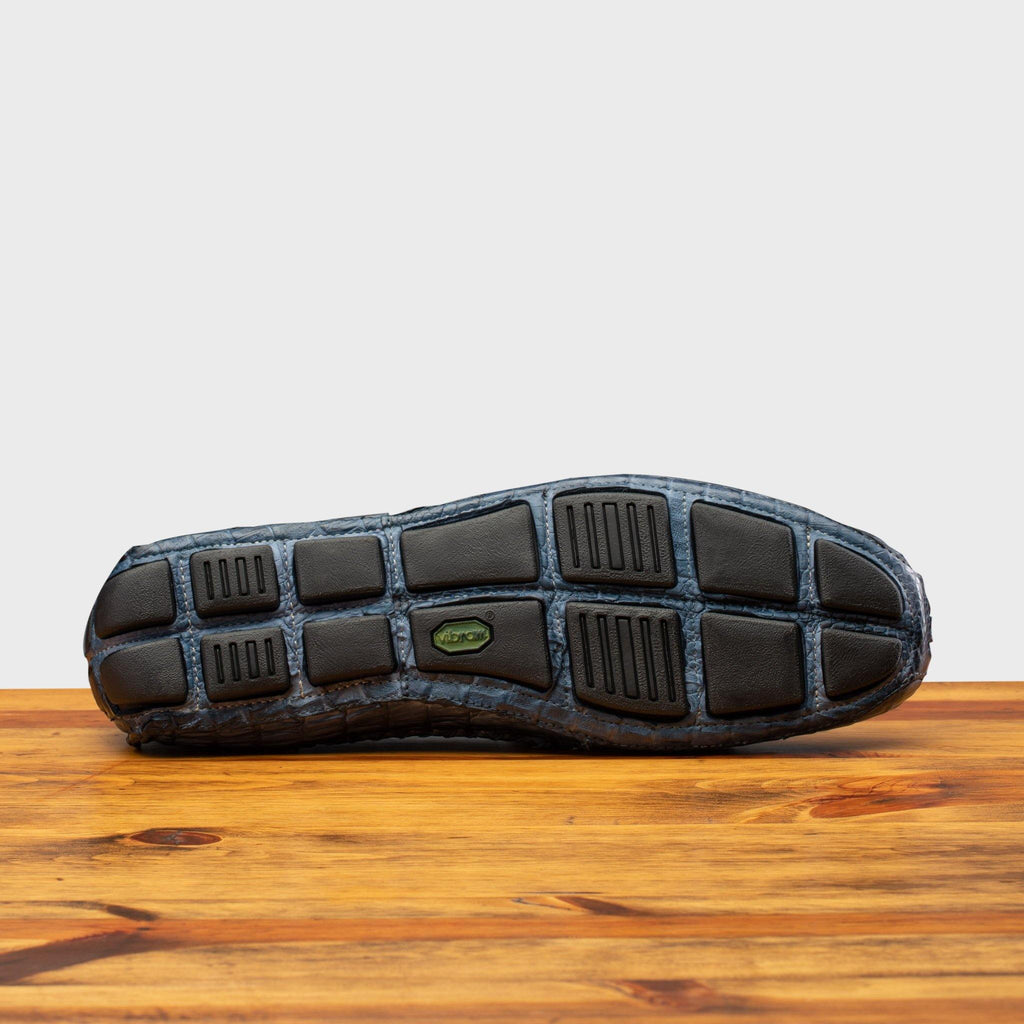 Full Rubber Vibram Outsole showing crocodile fully wrapped on the outsole of 4551 Calzoleria Toscana Denim Blue Dip-Dyed Driver on top of a wooden table