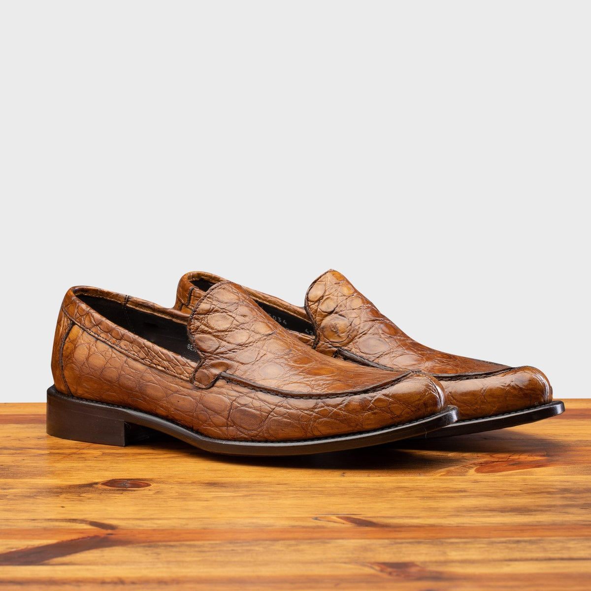 Pair of Mahogany leather loafer on a wooden surface with a light gray background