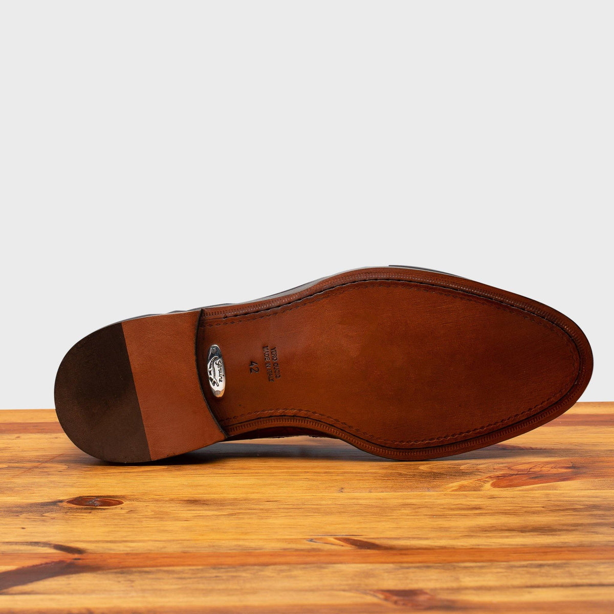 Outsole of Mahogany leather loafer on a wooden surface with a light gray background