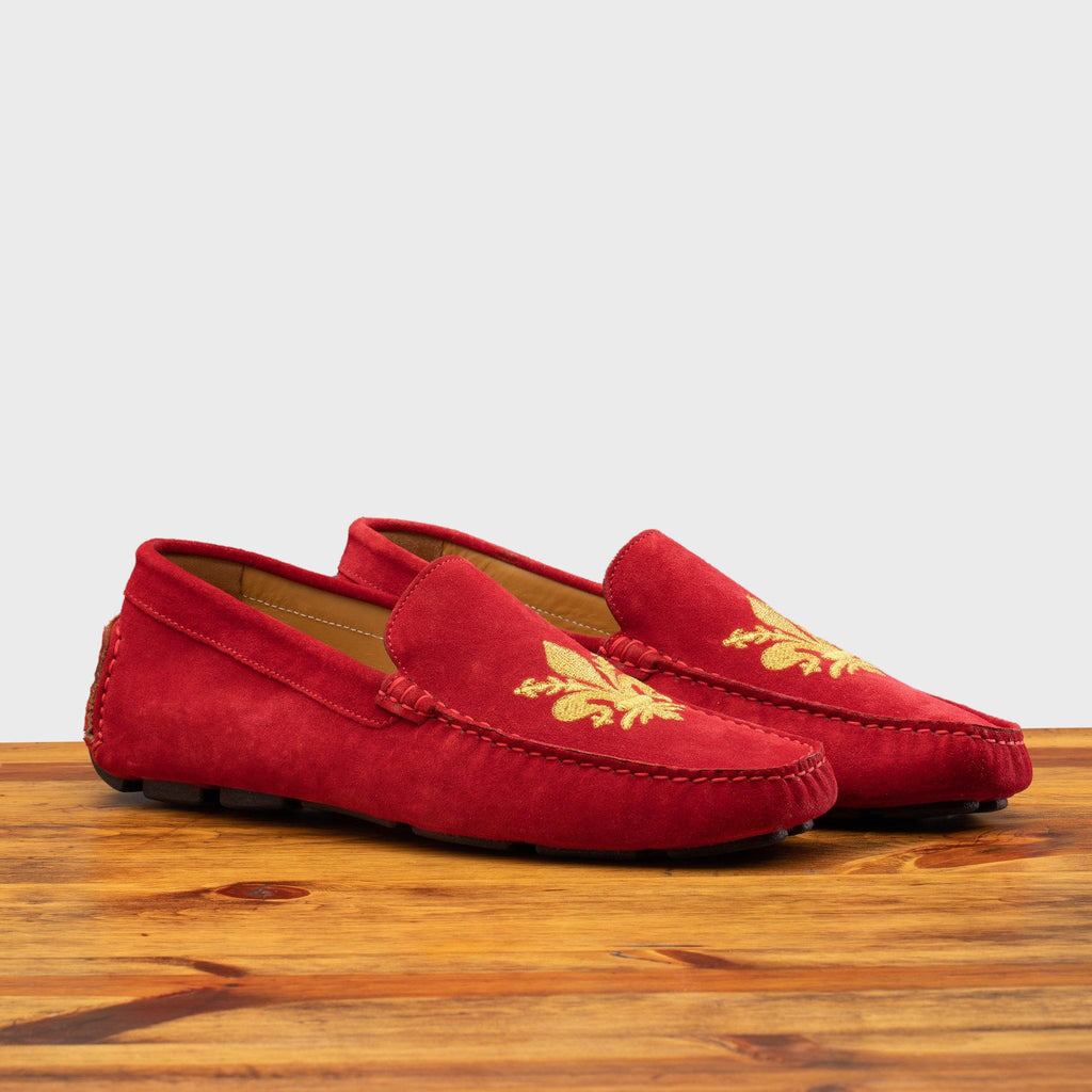 Pair of 5303 Calzoleria Toscana Red Venetian Suede Driver with gold embroidered fleur di Lis on top of a wooden table