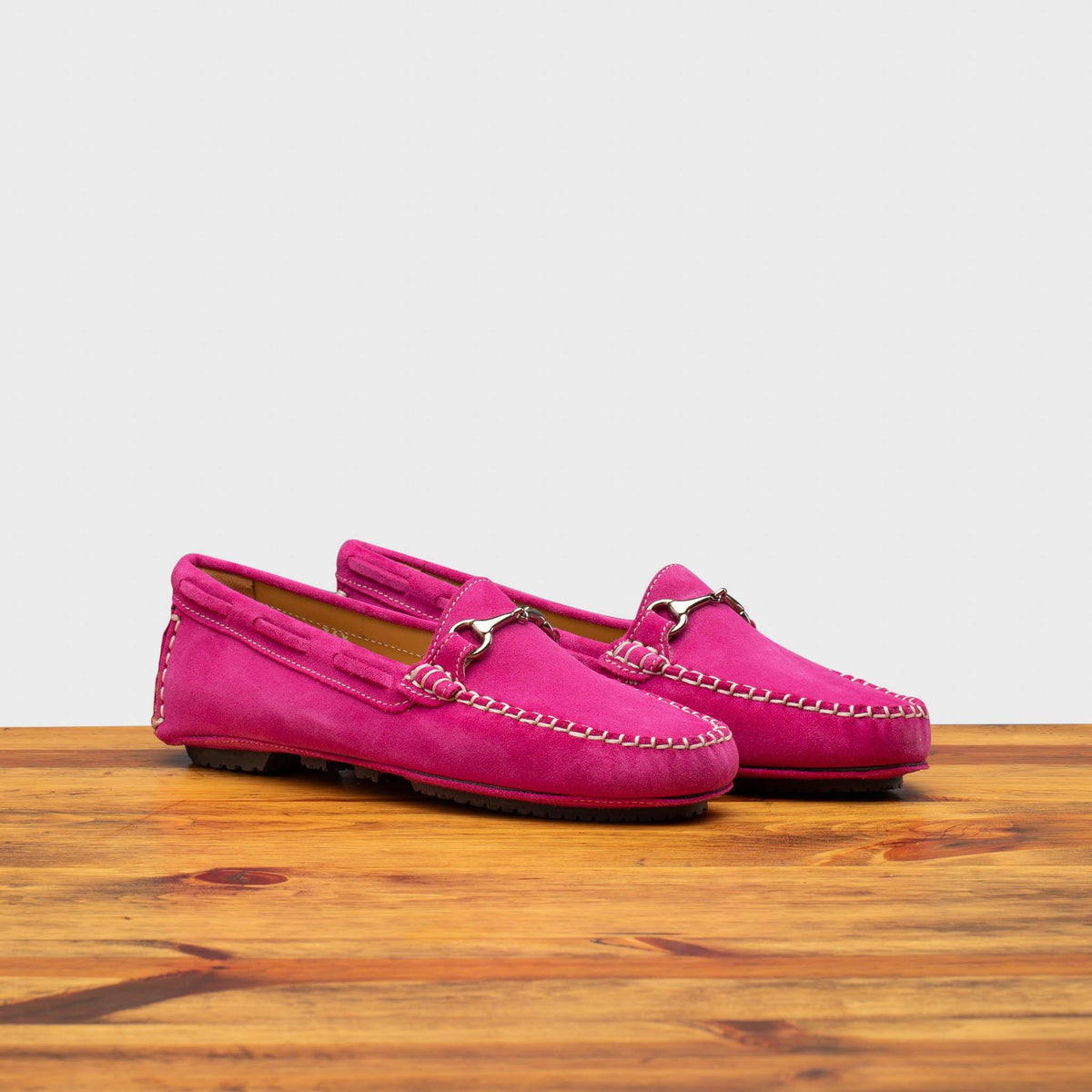 Pair of Fuchsia loafers on a wooden surface with a white background