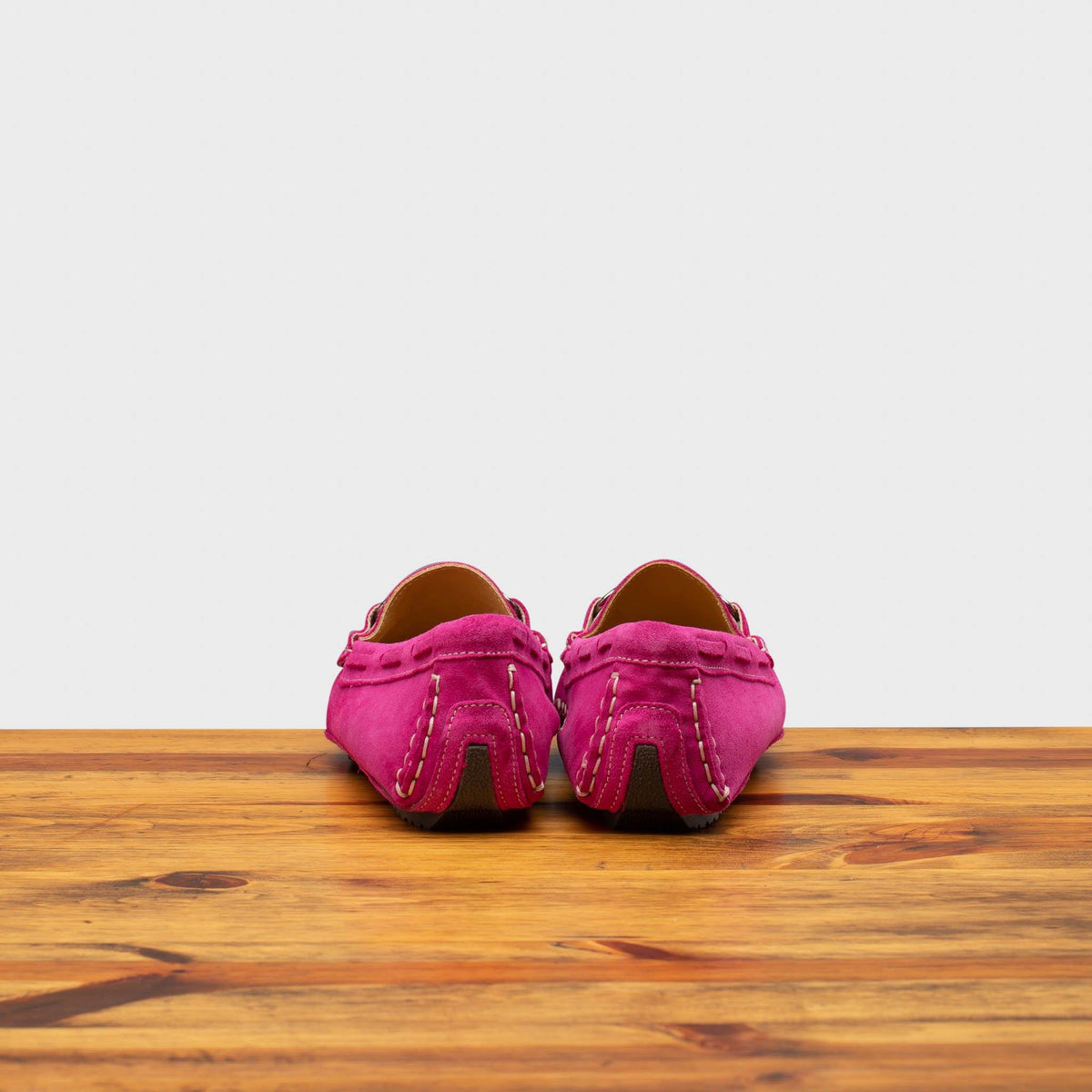 Back side of Fuchsia loafers on a wooden surface with a white background