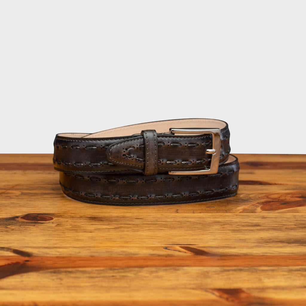 Full profile of C1482 Calzoleria Toscana Graphite Stitched Dress Belt curled on top of a wooden table