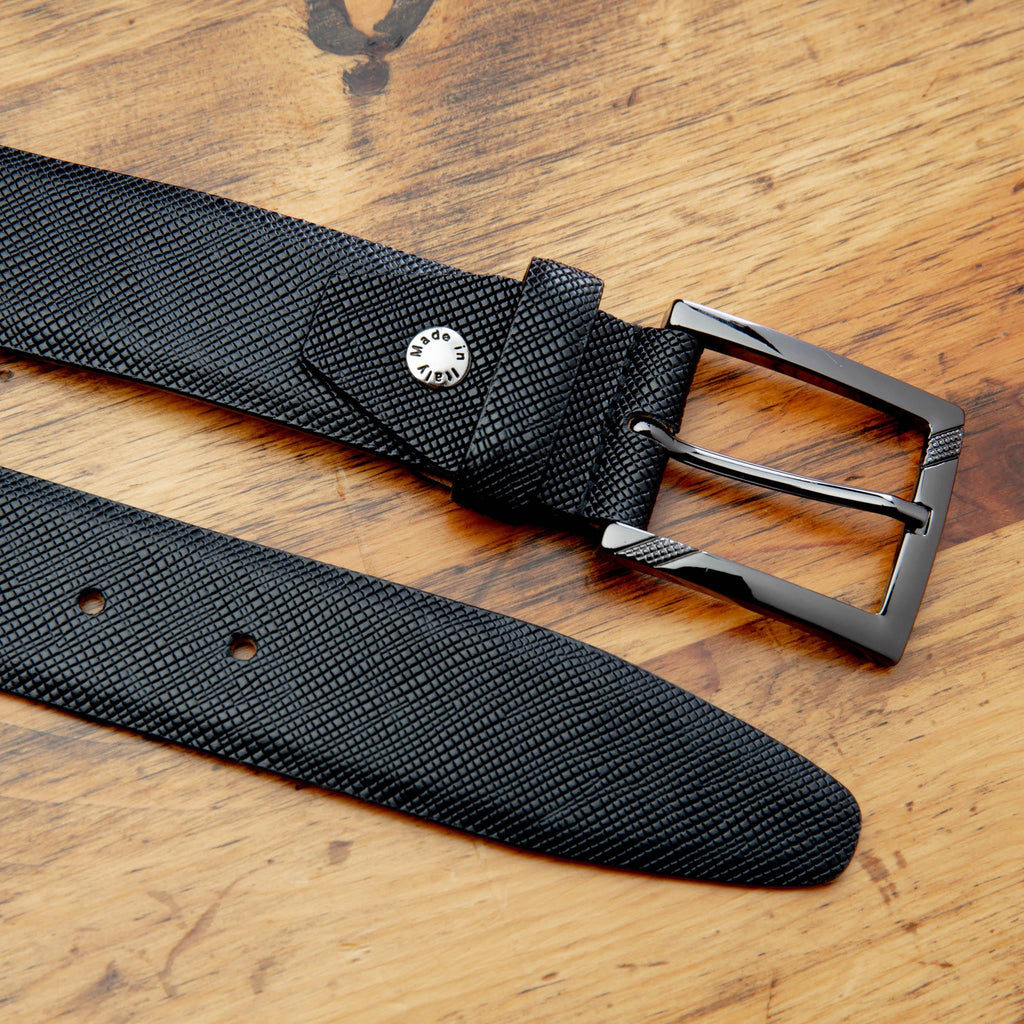 Up close picture of the nickle buckle and the cross hatch details of C1499 Calzoleria Toscana Black Saffiano Leather Belt on top of a wooden table
