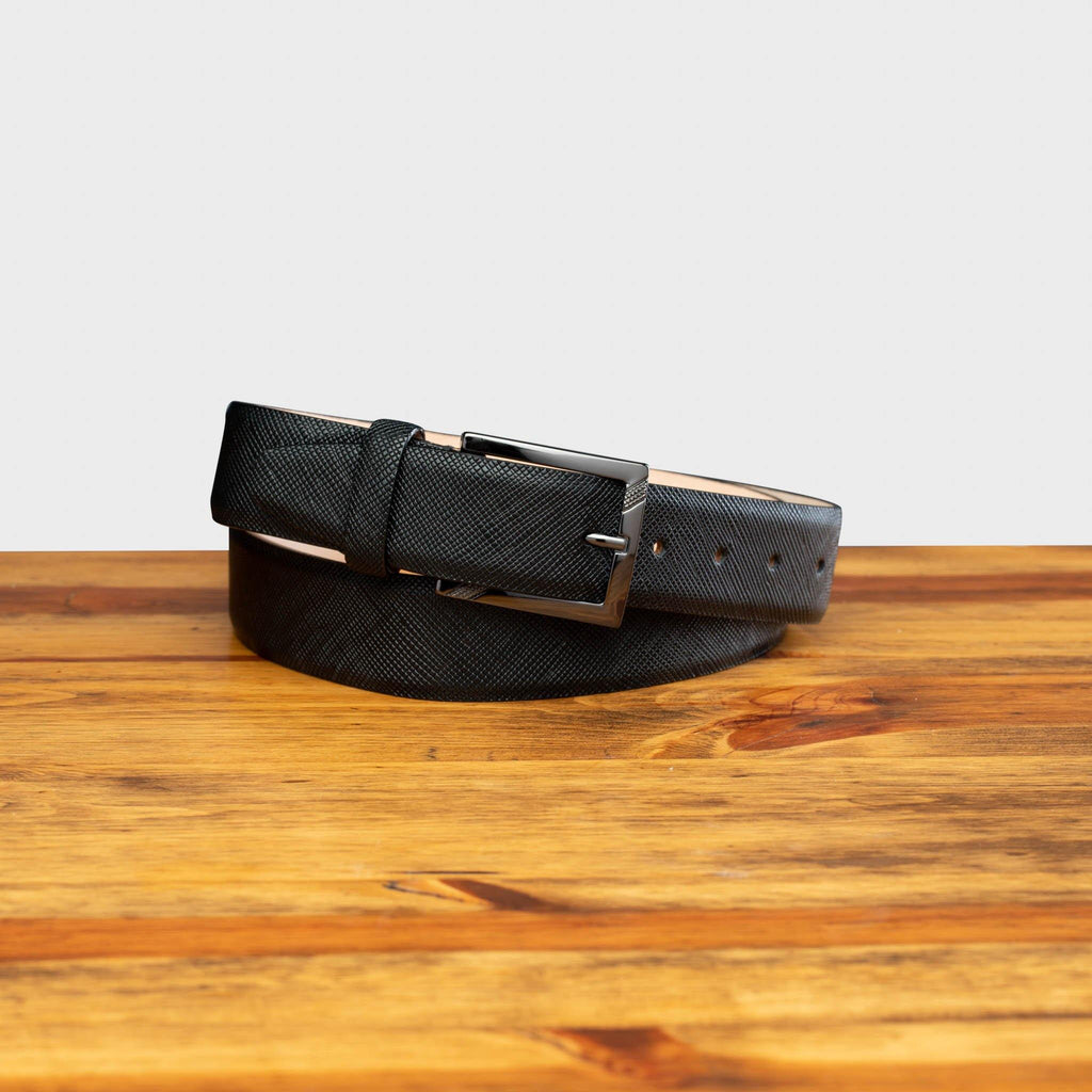 Front profile of  C1499 Calzoleria Toscana Black Saffiano Leather Belt curled on top of a wooden table