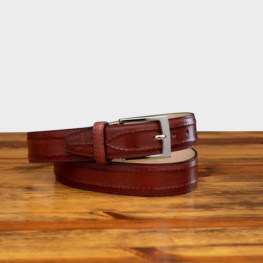 Front of C2216 Calzoleria Toscana Burgundy (Porpora) Inner Stitched Dress Belt curled up on top of a wooden table