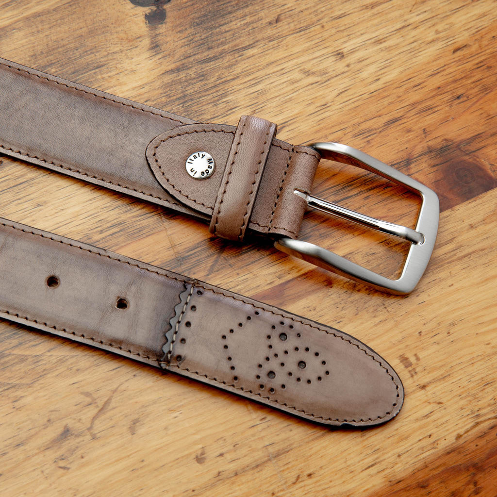 Up close picture of the silver buckle and perforated tip of C5677 Calzoleria Toscana Brown Artisan Dress Belt on top of a wooden table