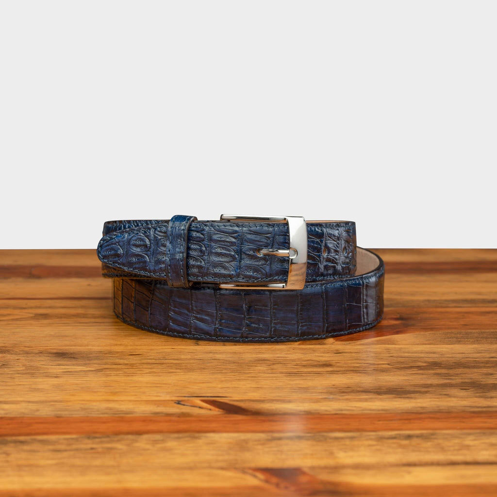 Front profile of C7981 Calzoleria Toscana Navy Exotic Hornback Belt curled up on top of a wooden table
