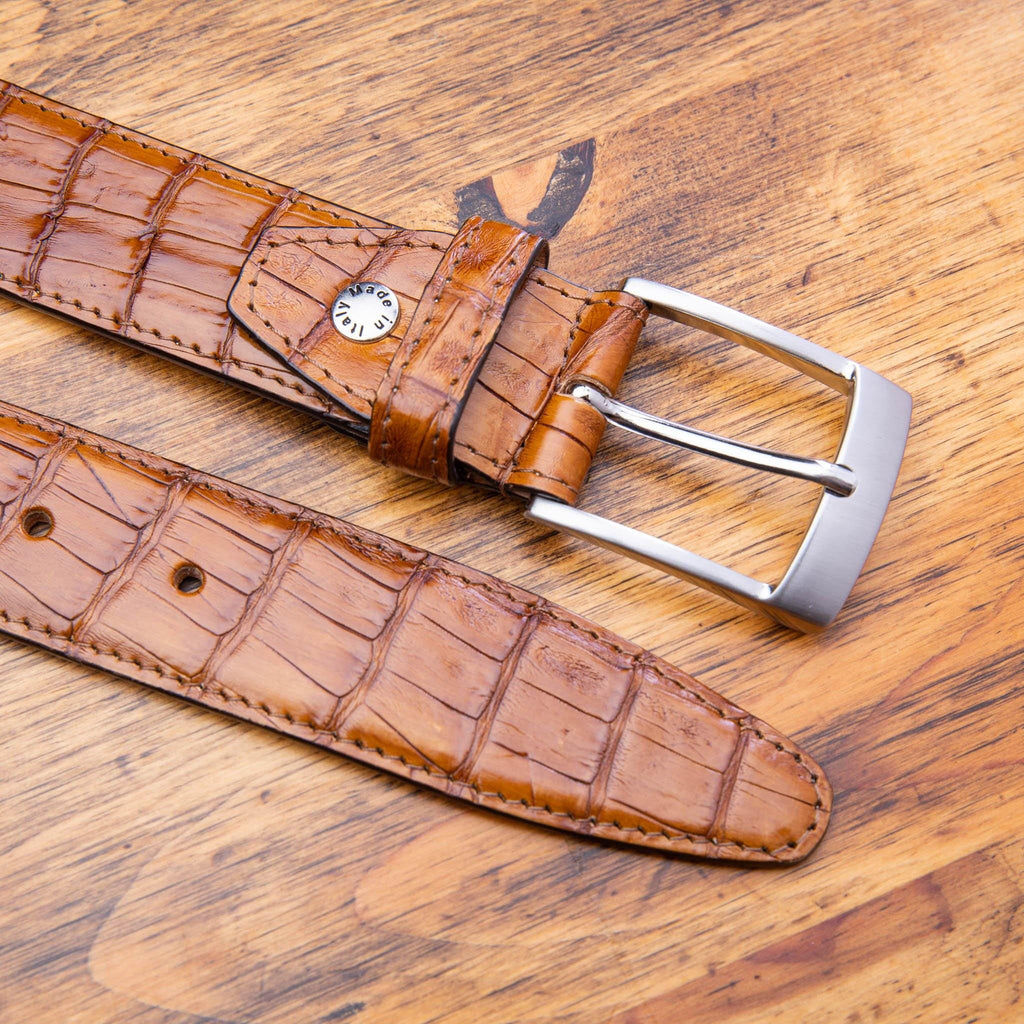 Up close picture of the silver buckle of C7981 Calzoleria Toscana Brick Exotic Hornback Belt on top of a wooden table