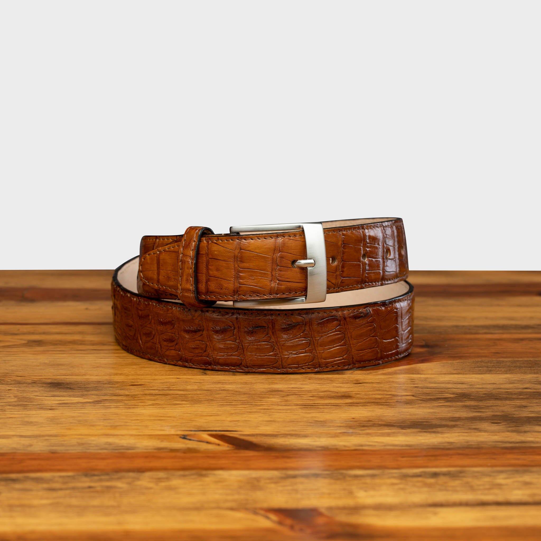 Front profile of C7981 Calzoleria Toscana Brick Exotic Hornback Belt curled up on top of a wooden table