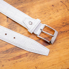 Up close picture of the silver buckle of C7981 Calzoleria Toscana White Exotic Hornback Belt on top of a wooden table
