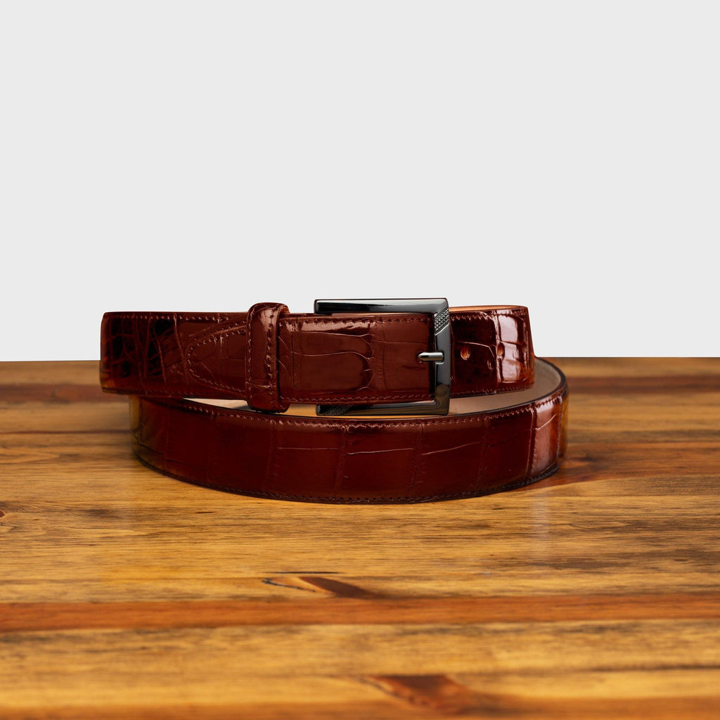 Front profile of C8099 Calzoleria Toscana Burgundy Crocodile Belt on top of a wooden table