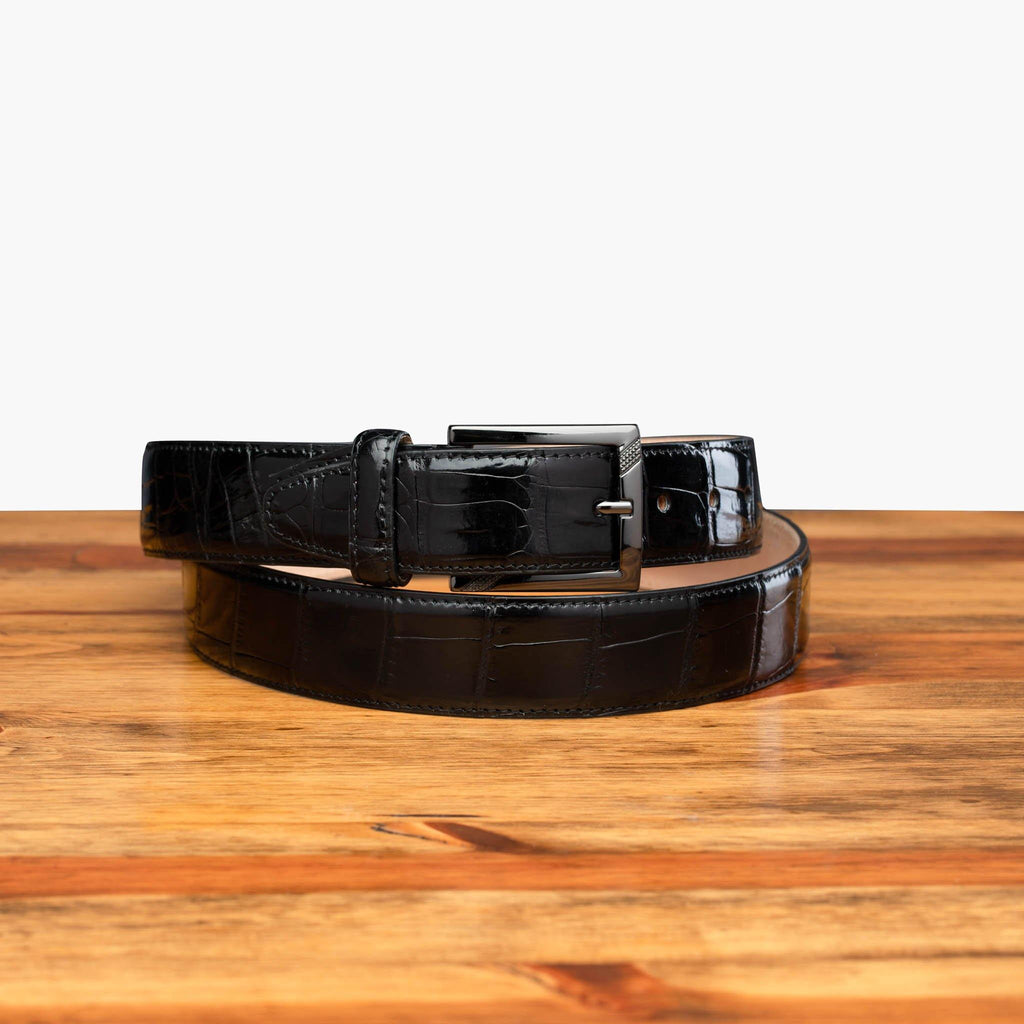 Front profile of C8099 Calzoleria Toscana Black Crocodile Belt curled up on top of a wooden table
