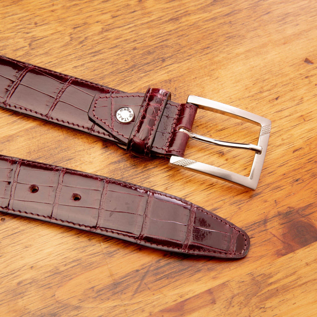 Up close picture of the silver buckle of C8099 Calzoleria Toscana Burgundy Crocodile Belt on top of a wooden table