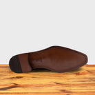 Outsole of a Chestnut, wholecut blucher dress shoe with a lace-up closure, displayed on a wooden surface.